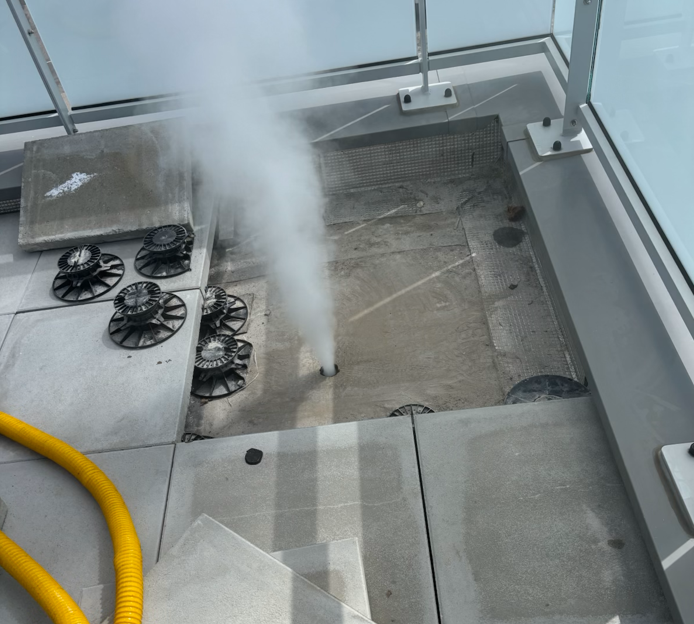 Technicien effectuant une recherche de fuite avec de la fumée blanche s’échappant d’un balcon.
